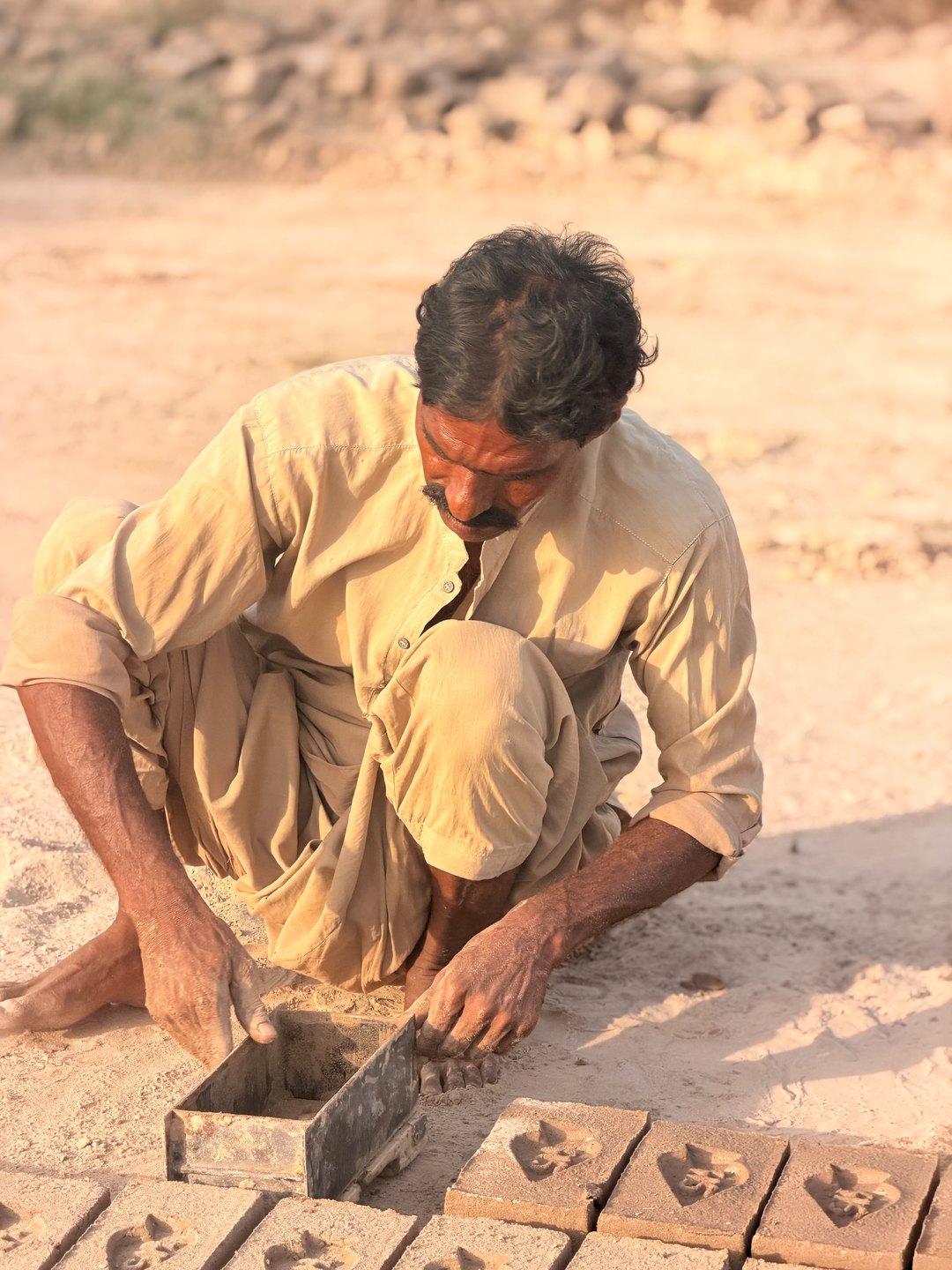 Arshad presses clay into a metal brick mold