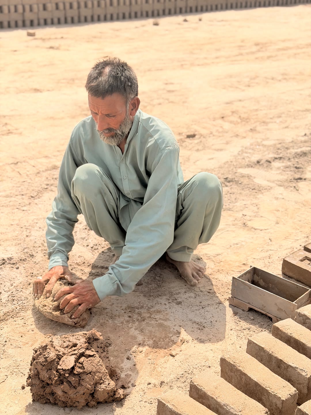 Khalid Masih squats barefoot and shapes a ball of clay at the brick kiln