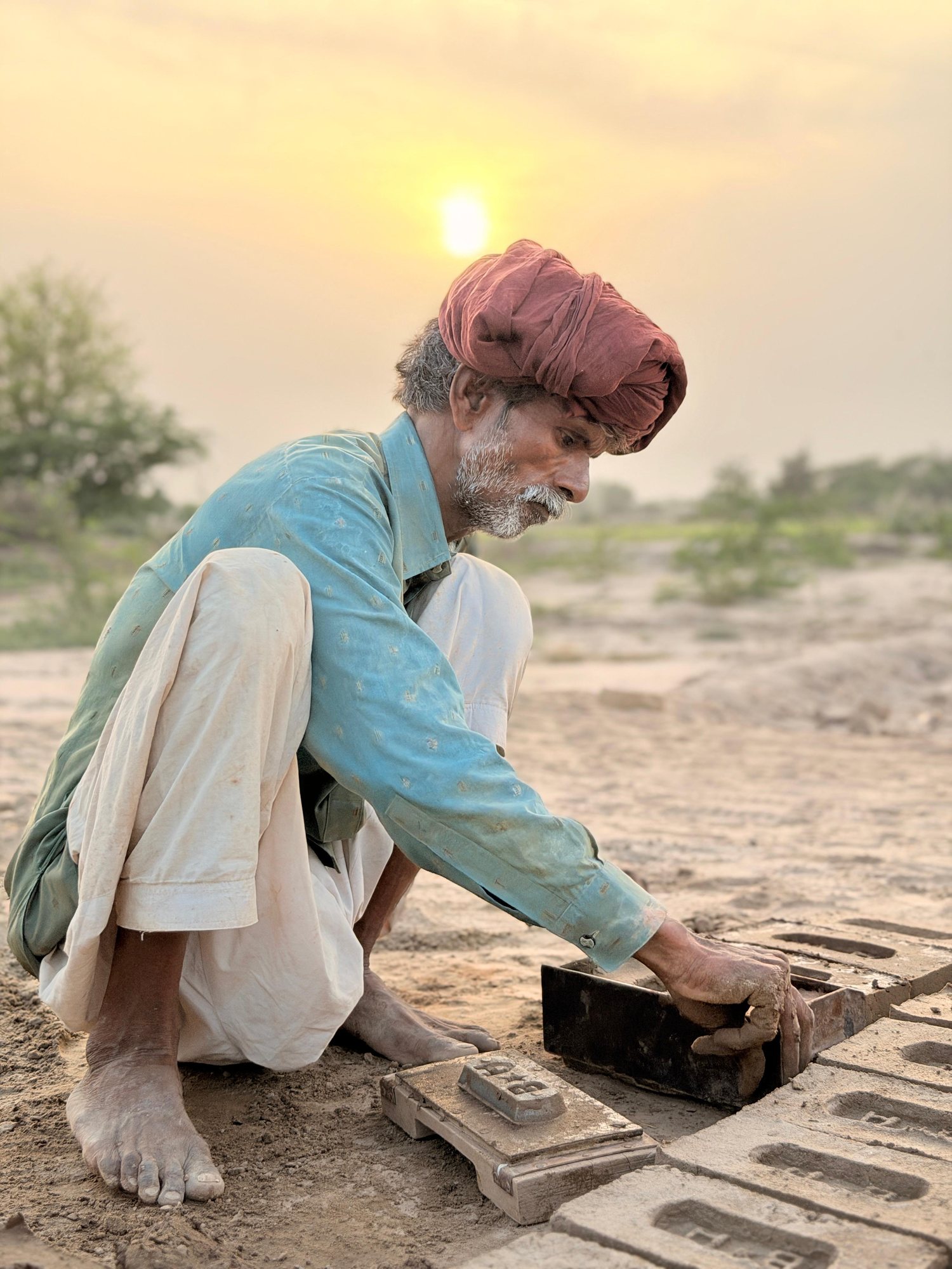 A man at a brick kiln setting wet clay into a mold